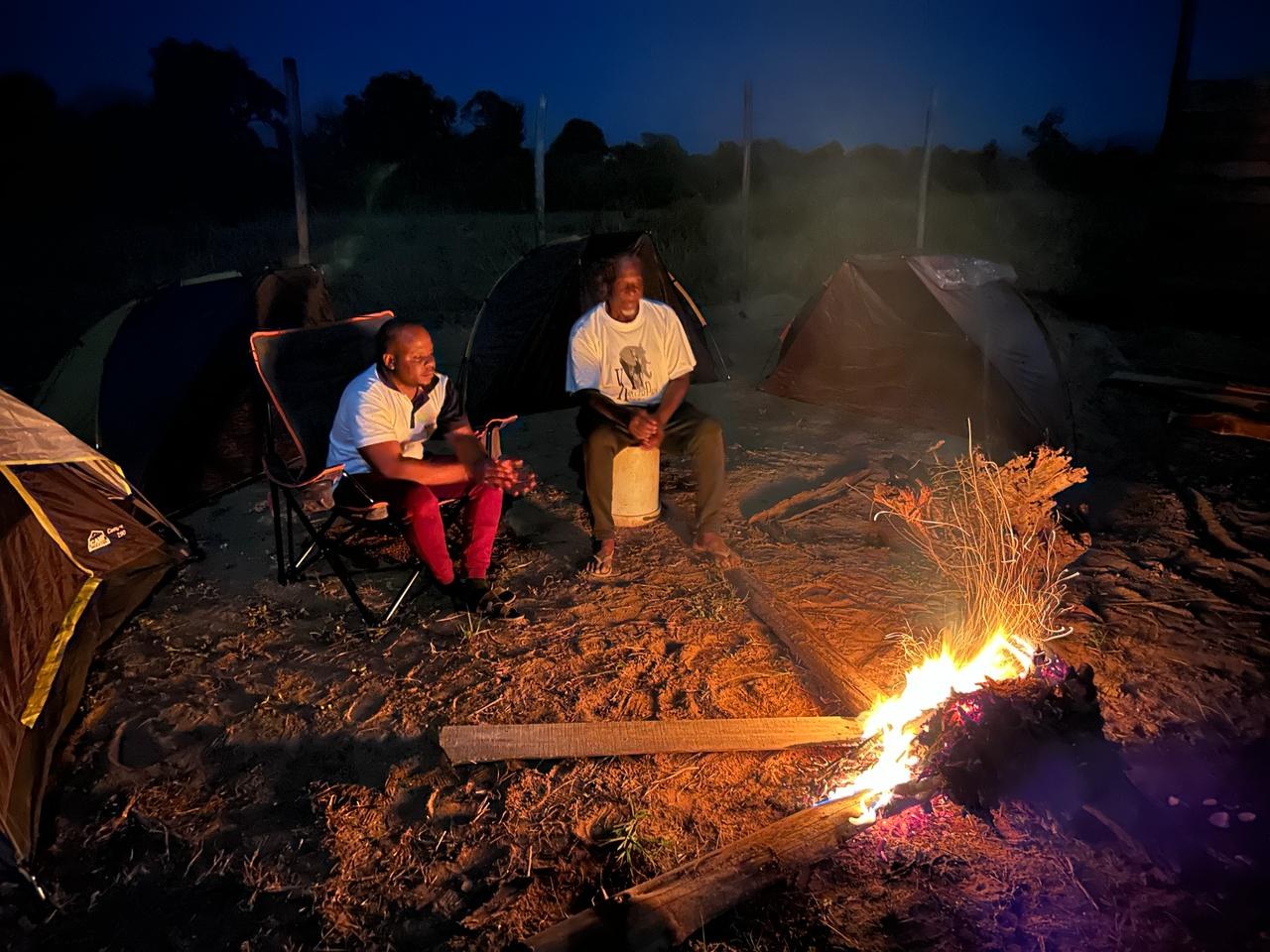 Two people sharing fellowship beside a campfire and tents during an outdoor ministry gathering